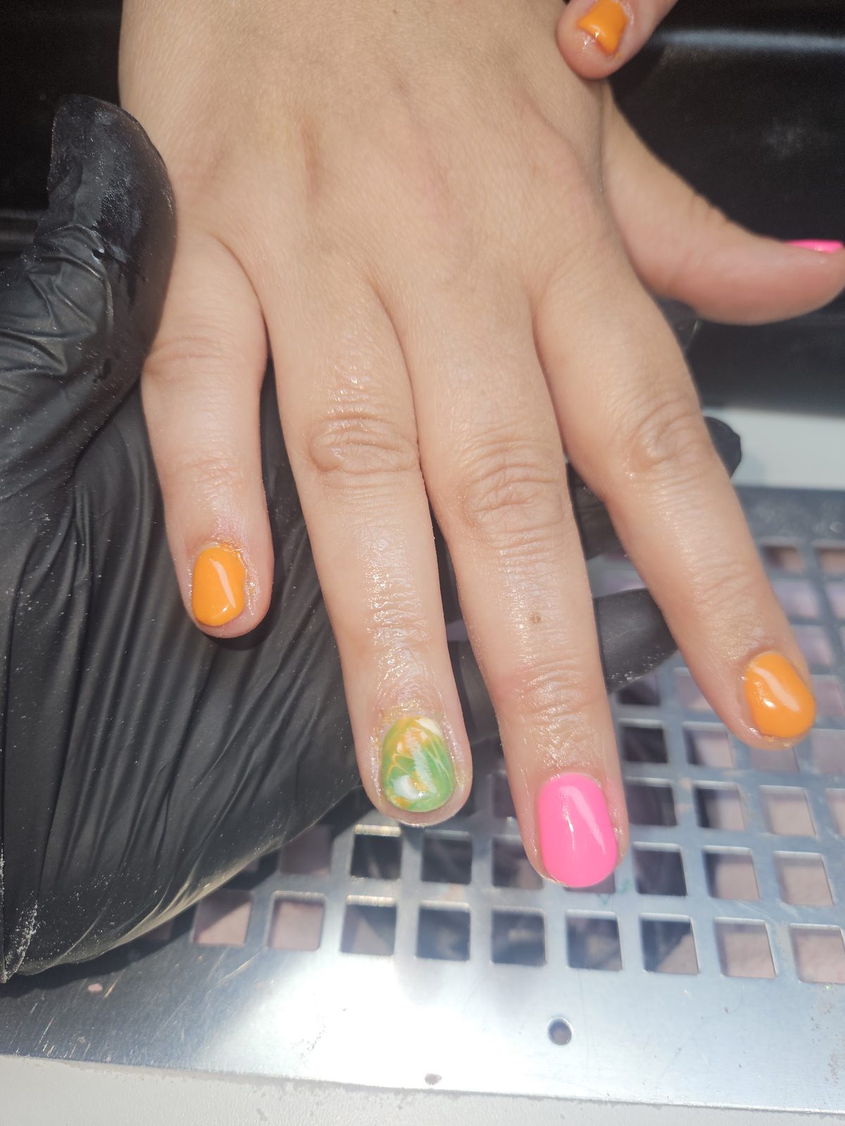 Rieanda houdt met een zwarte handschoen de hand van een klant vast, nagels in oranje, roze en groen