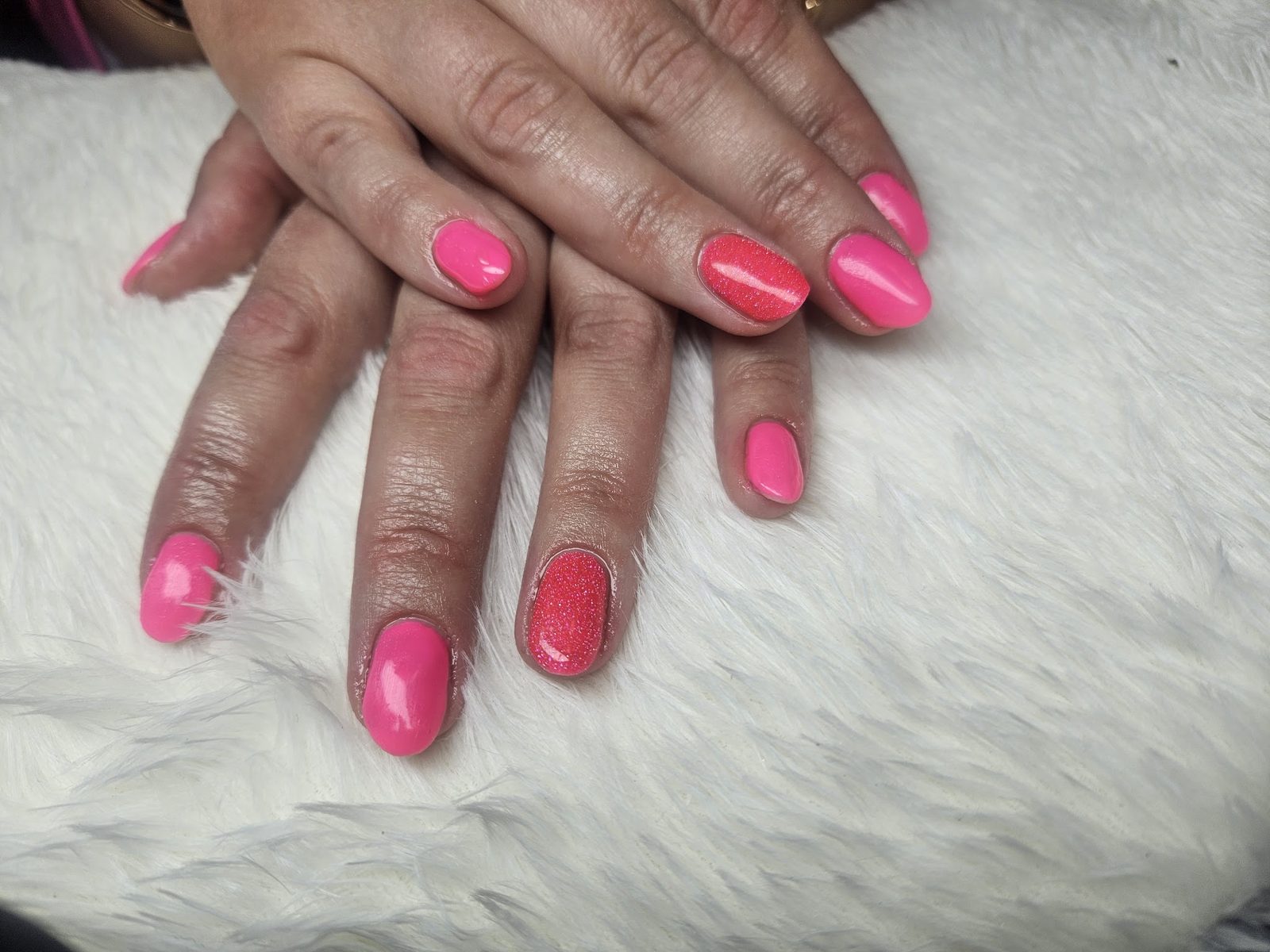 Neonroze gelpolish met één rode glitternagel, op een witte vacht